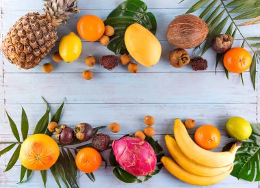 Sağlıklı gökkuşağı tropikal meyve çerçeve ile palmiye yaprakları mavi ahşap masa, üstten görünüm, kopya alanı
