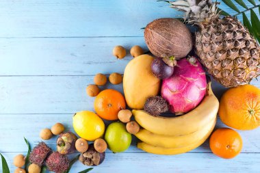 Sağlıklı gökkuşağı tropikal meyve çerçeve ile palmiye yaprakları mavi ahşap masa, üstten görünüm, kopya alanı