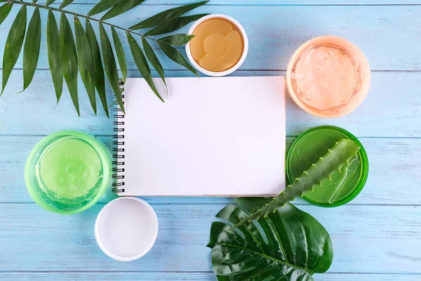 gel of snail, eye patch and Aloe Vera Gel in jar with paper notebook on blue wooden background. Flat lay