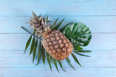 Ananas ve tropikal palmiye yaprakları mavi ahşap arka plan üzerinde. Yaz konsepti. Yaratıcı düz lay kopya alanı ile.