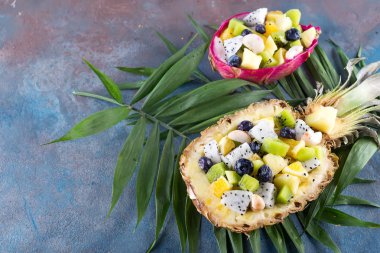 Yarım bir ananas taş zemin üzerine palmiye yaprakları üzerinde servis egzotik meyve salatası