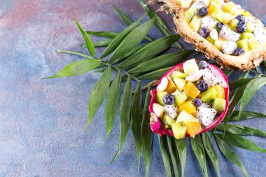 Ekzotik meyve salatası yarım bir ejderha meyvesi ve ananas ile servis edilir taş zemin üzerinde palmiye yaprağı, kopyalama alanı.