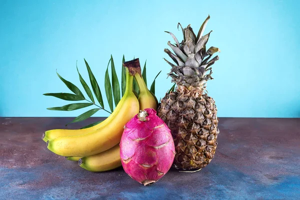 Assorted tropical fruits pineapple, mango, dragon fruit, on stone background. Group of exotic tropical fruits. Vegetarian healthy concept, copy space