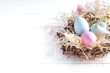 Beyaz ahşap arka planda, kopya alanı ile küçük yuvadaki renkli Paskalya yumurtaları. Tatil olay