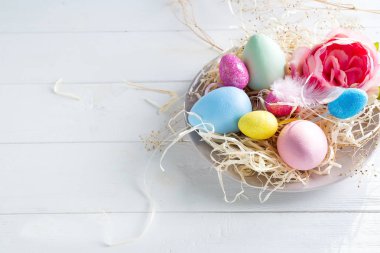 Beyaz ahşap arka planda, kopya alanı ile küçük yuvadaki renkli Paskalya yumurtaları. Tatil olay