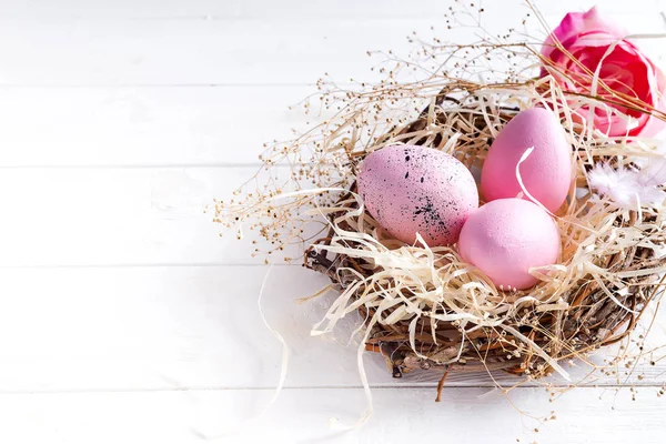 Huevos de Pascua rosa en nido pequeño con sobre fondo de madera blanca, espacio de copia —  Fotos de Stock