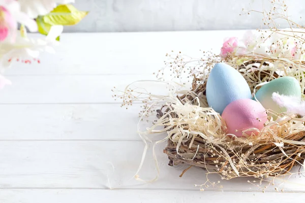 Schöne Blume mit bunten Eiern im Nest auf hellem Hintergrund. Frühjahrs- und Osterferienkonzept mit Kopierraum. — Stockfoto