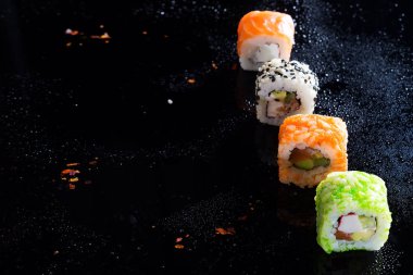 Suşi, bir sürü kümeleriyle renkli suşi roll. Su damlaları siyah bir zemin üzerine şık suşi ayarlar. Kopya alanı düz yatıyordu