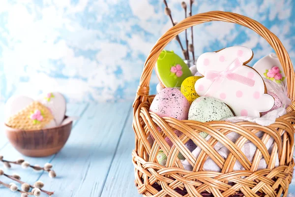 五颜六色的复活节彩蛋和釉面饼干在篮子在蓝色木制背景 — 图库照片
