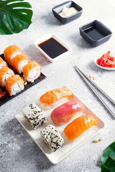 Various sushi on ceramic plate with metal Korean sticks on light stone background with green leaves, flat lay copy space — Stock Photo, Image