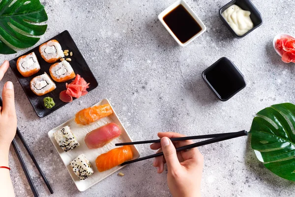 Varios sushi fresco y delicioso conjunto en pizarra blanca y negra con palos de metal y pizarra, salsa y mano sobre fondo de piedra clara, plano laico — Foto de Stock