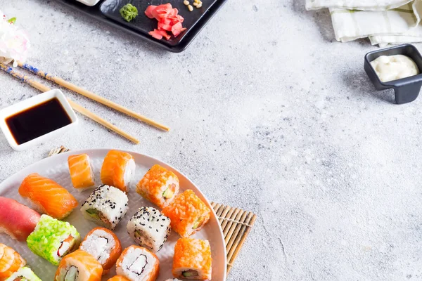 Varios sushi fresco y delicioso establecido en pizarra blanca con palos de madera, salsa sobre fondo de piedra clara, puesta plana — Foto de Stock