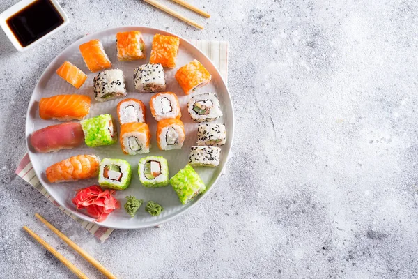 Varios sushi fresco y delicioso establecido en pizarra blanca con palos de madera, salsa sobre fondo de piedra clara, puesta plana — Foto de Stock