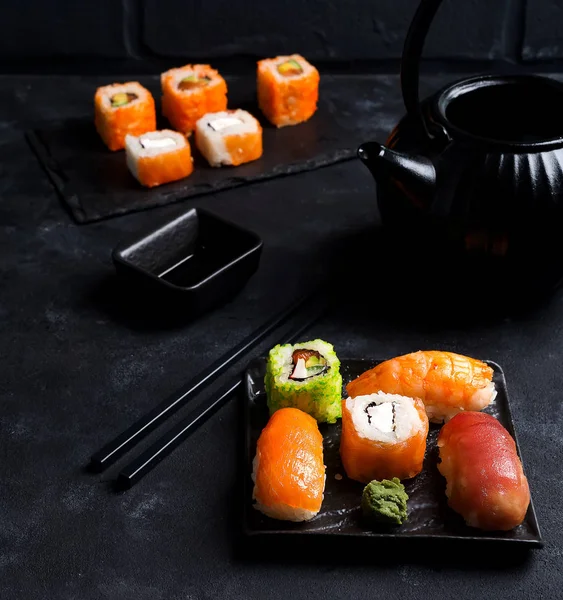 Asian food background with black iron teapot and sushi set on slate plate on black stone table