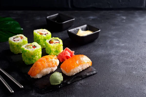 Siyah barut barut sopa, sos ve düz siyah taş zemin üzerine nori ile ayarlamak çeşitli taze ve lezzetli suşi yatıyordu