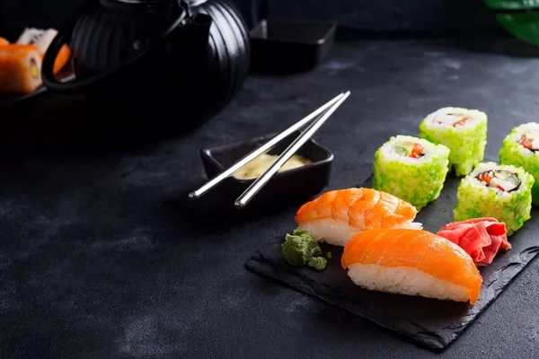 Asian food background with black iron teapot and sushi set on slate plate on black stone table