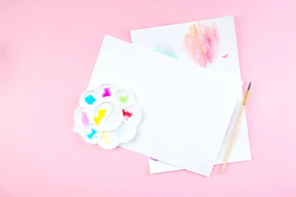 La maqueta del cuaderno para la obra de arte con las pinturas de acuarela, la paleta y los pinceles. Vista desde arriba. Herramientas de trabajo artístico sobre mesa rosa . — Foto de Stock