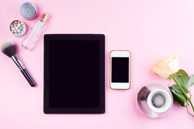 Kahveli kadın işyeri, tabletli telefon ve kozmetik ürünlü güller. Pembe arkaplanda üst görünüm, maket