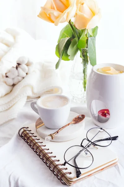 Kaffeebecher mit Gläsern auf dem Notizbuch, Kerze und Rose auf einem weißen Bettaufsatz. Frau gemütlich am Morgen — Stockfoto