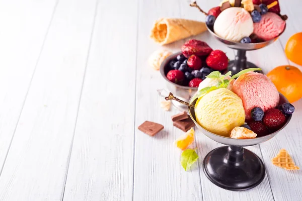 Set de cucharadas de helado de diferentes colores y sabores con bayas, chocolate sobre fondo de madera — Foto de Stock