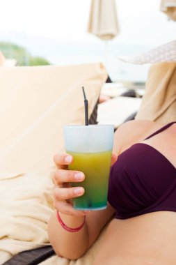 Genç ve güzel bir kadın yüzme havuzunun yanında yaz kokteyli içer yaz tatilinin tadını çıkarır, plajda dinlenir.,