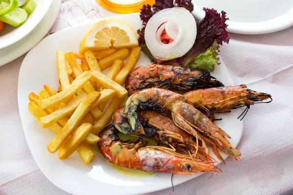 Close up big size grill shrimps with fried potato, vegetables and lemon, lunch time in restaurant.