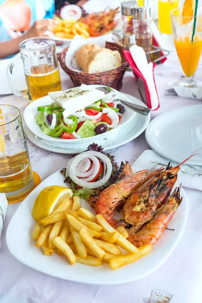 Plate with fresh greek salads, shrimp, potato fried, beers and bread, olive oil on a table. Traditional Greek dish. — Stock Photo, Image