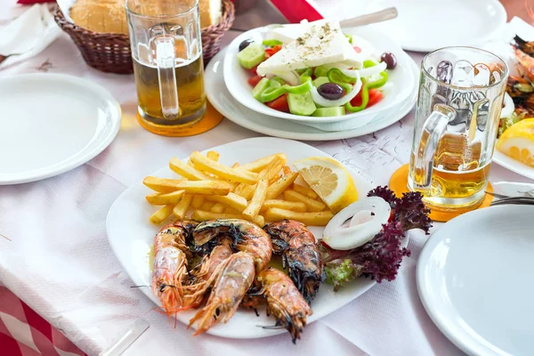 Plato con ensaladas griegas frescas, camarones, papas fritas, cervezas y pan, aceite de oliva en una mesa. Plato griego tradicional . — Foto de Stock