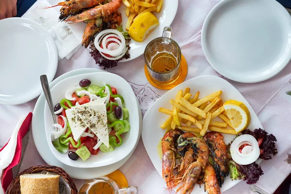 Plato con ensaladas griegas frescas, camarones, papas fritas, cervezas y pan, aceite de oliva en una mesa. Plato griego tradicional . — Foto de Stock