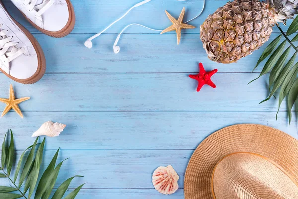 Summer flat lay background. Palm leaves, shoes, pineapple, headphones, hat and starfish on blue woodwn background.