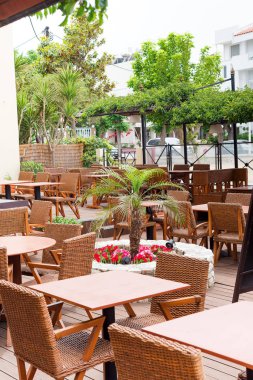 Kos, Yunanistan - 23 Mayıs 2019: Küçük palmiye ağacı ile plastik tencere ile rahatlatıcı tatil tatiliçin Cafe ahşap masalar