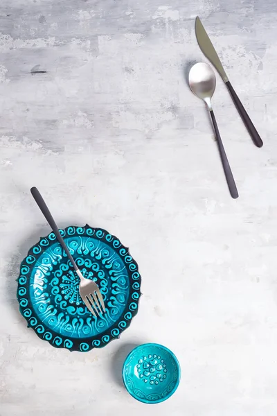 Türkische Keramik dekoriert blauen Teller und Schüssel mit neuem schwarzen Luxusbesteck auf Steinhintergrund, Draufsicht — Stockfoto