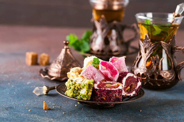 Bowl with various pieces of turkish delight lokum and black tea with mint on a dark background