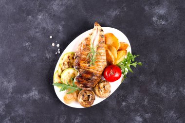 Domatesli ızgara tavuk göğsü, taştan bir arka planda mantar, düz uzanmış.