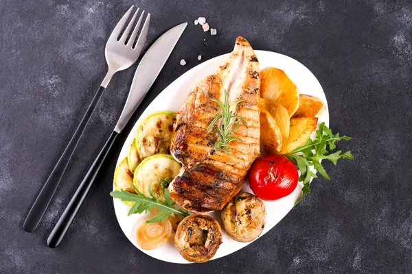 Grilled chicken breast on a plate with tomatoes, asparagus and mushrooms on a stone background, flat lay — Stock Photo, Image