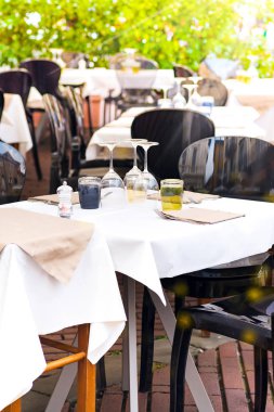 Masaları ve sandalyeleri olan bir kahve terası manzarası. Kutlama ve randevu için şık bir ortam. Şarap kadehleri, masanın üzerindeki peçeteler, güneşli bir günde sokak kafesi.