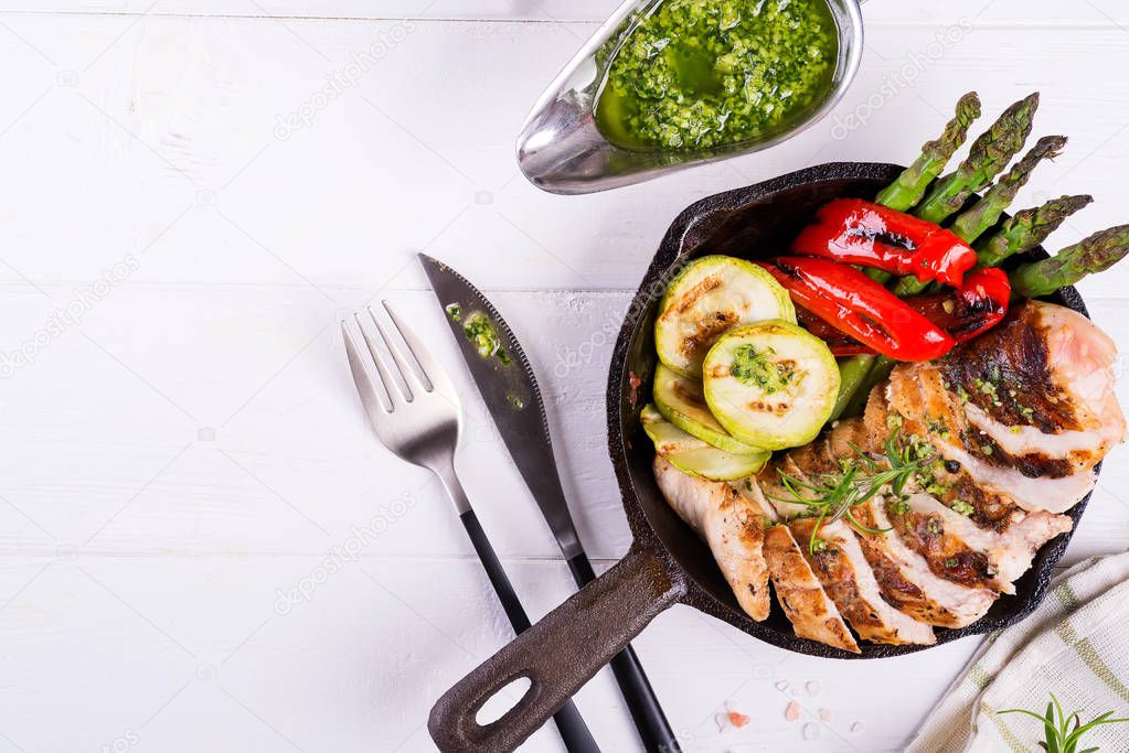 Grilled chicken breast on a cast iron skillet with grill vegetables on a wooden background, flat lay