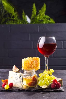 Taş arka planda gözlük kırmızı şarap ile peynir, çilek ve üzüm çeşitleri. Kopyalama alanı