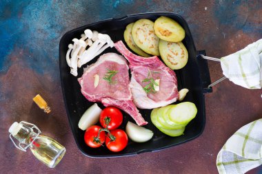 Beton bir arka plan üzerinde ızgara tavada taze sebze ile kemik çiğ domuz eti, üst görünümü