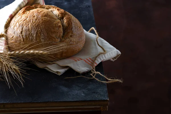 Okrągły świeżo pieczone rustykalne żyto chleb okrągły z uszy pszenicy i serwetki na ciemnym tle, Kopiuj przestrzeń — Zdjęcie stockowe