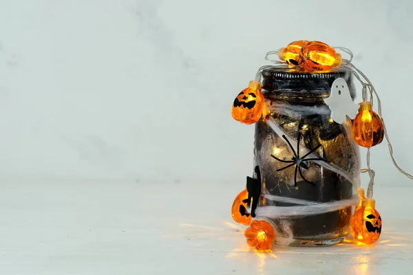 Pot rempli de lumières à ficelle orange dans une pièce sinistre pleine d'un pot noir avec une toile et une araignée sur un fond clair — Photo