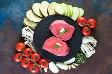 Koyu taş arka plan üzerinde bir tavada taze sebze ile kemik çiğ sığır eti biftek, üst görünümü