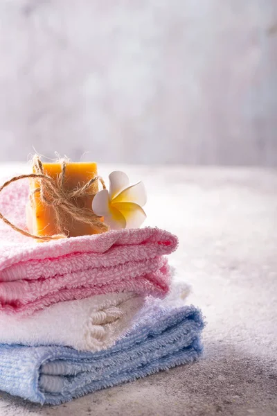 Wiele kolorowych ręczników kąpielowych ułożonych na siebie z mydłem ręcznym i kwiatem na jasnym tle kamiennym, przestrzeń kopiowania — Zdjęcie stockowe