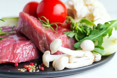 Mermer arka planda tavada taze sebzeli çiğ biftek.