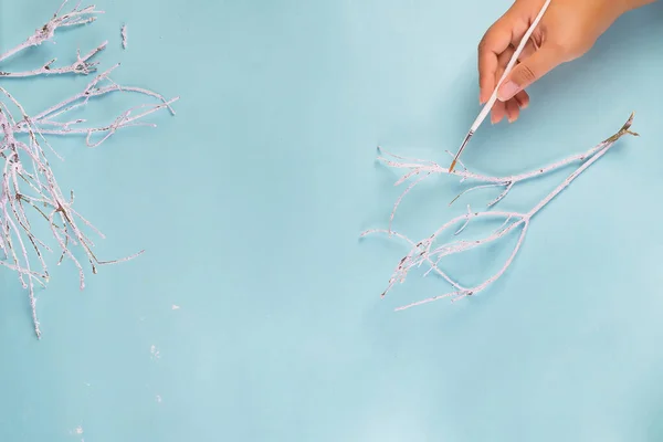 La mano de las mujeres decora ramita de árbol en nieve blanca sobre un fondo azul con espacio de copia, disposición plana —  Fotos de Stock