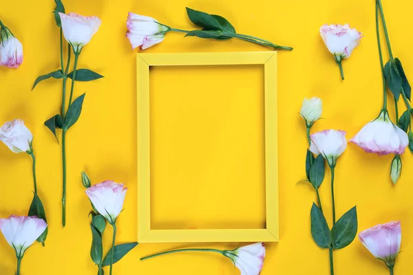 Empty yellow frame and flowers eustoma as layer on yellow paper background with copy space. Holiday concept