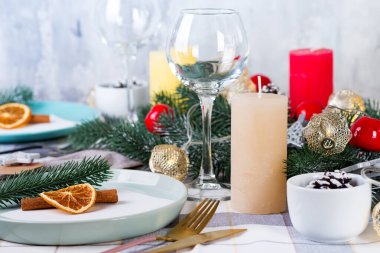 Gri bir tekstil üzerinde kuru portakal ve tarçınlı Noel ve yeni yıl sofrası. Çam kozalakları, dallar ve mumlarla süslenmiş yemek salonu.