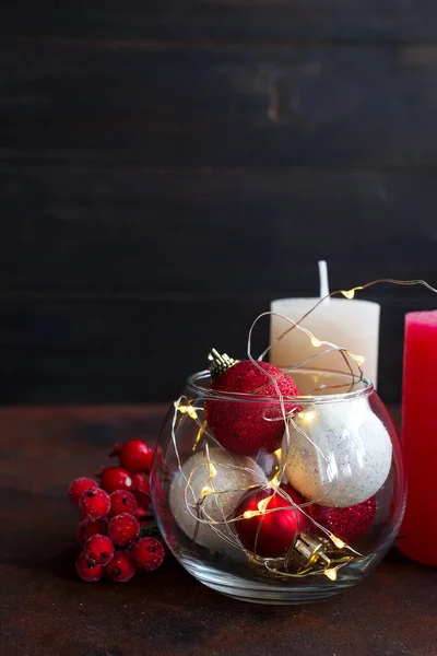 Bola de Natal vermelha e branca em um frasco de vidro, velas coloridas e bagas em um fundo de pedra escura com espaço de cópia — Fotografia de Stock