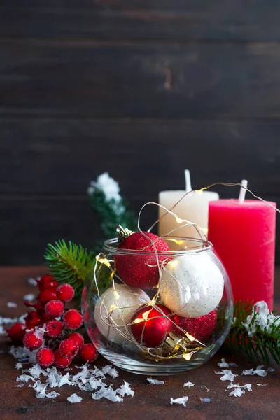 Bola de Natal vermelha e branca em um frasco de vidro, velas coloridas, ramos de abeto e bagas em um fundo de pedra escura com espaço de cópia — Fotografia de Stock