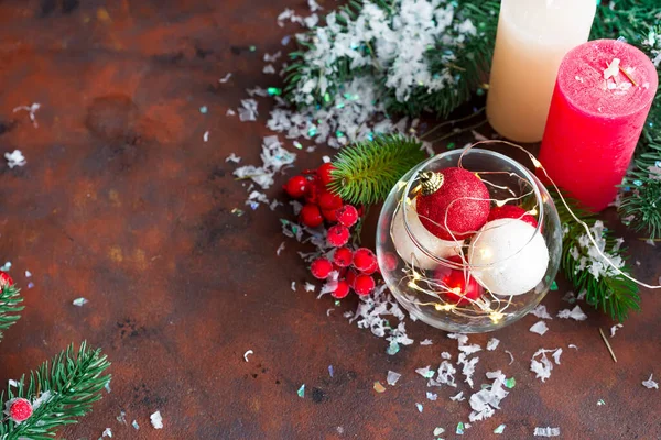 Bola de Natal vermelha e branca em um frasco de vidro, velas coloridas, ramos de abeto e bagas em um fundo de pedra escura com espaço de cópia — Fotografia de Stock